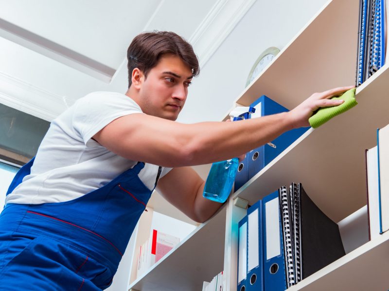 Male office cleaner cleaning shelves in office